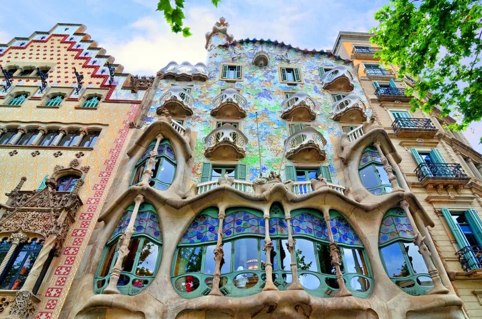 The colorful mosaic facade and curved balconies of Casa Batllo seen from street level on Passeig de Gracia.
